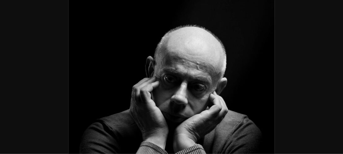 A man resting his face in his hands against a dark background, conveying the quiet weight and isolation of leadership